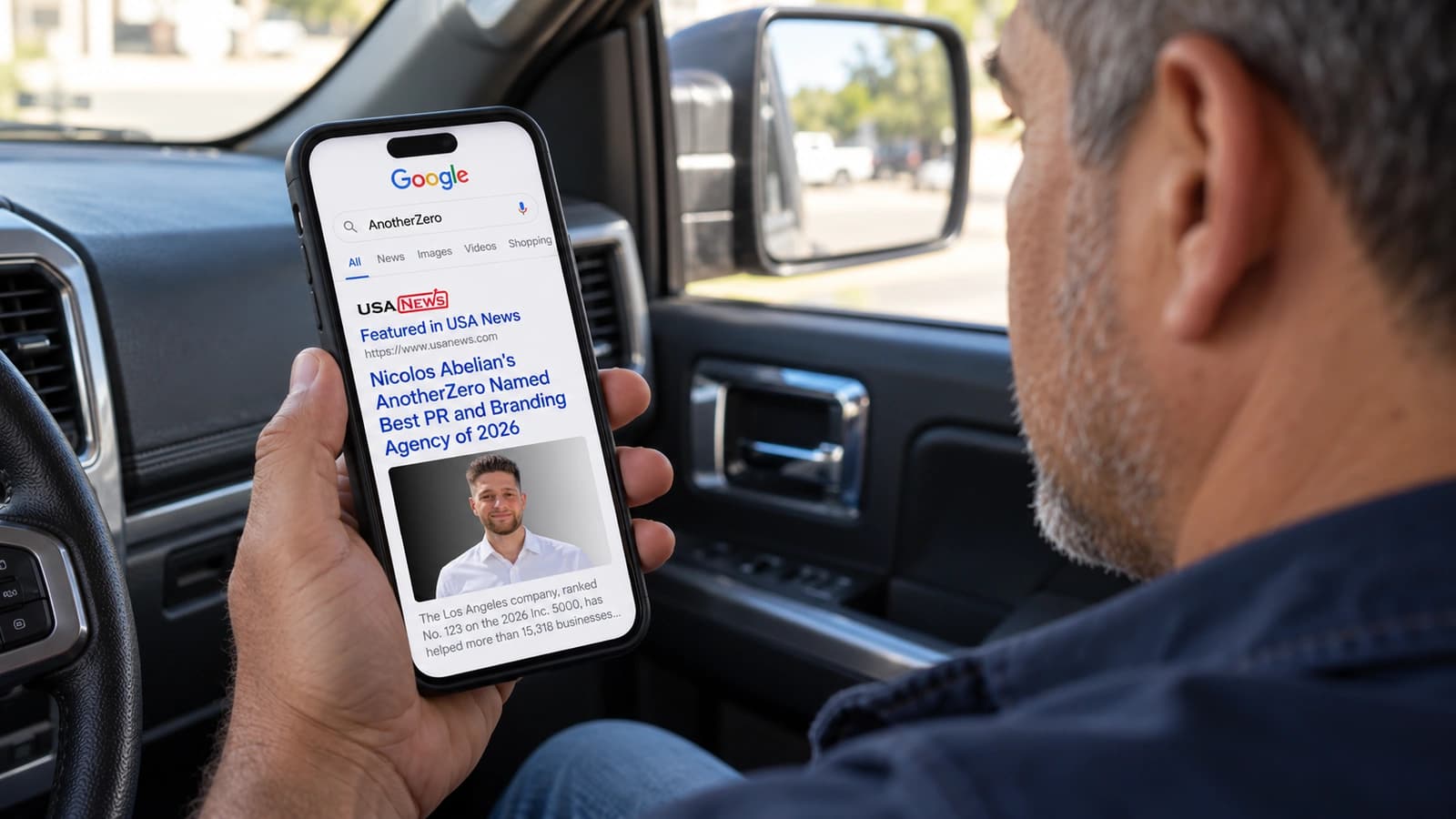 A man in a parked pickup sees an AnotherZero feature in USA News in a Google search on his phone.